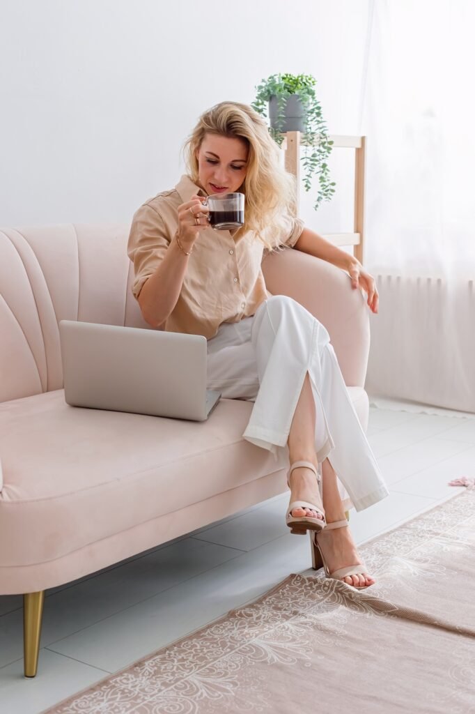 A blonde business woman, working on laptop on sits on sofa with cofee cup